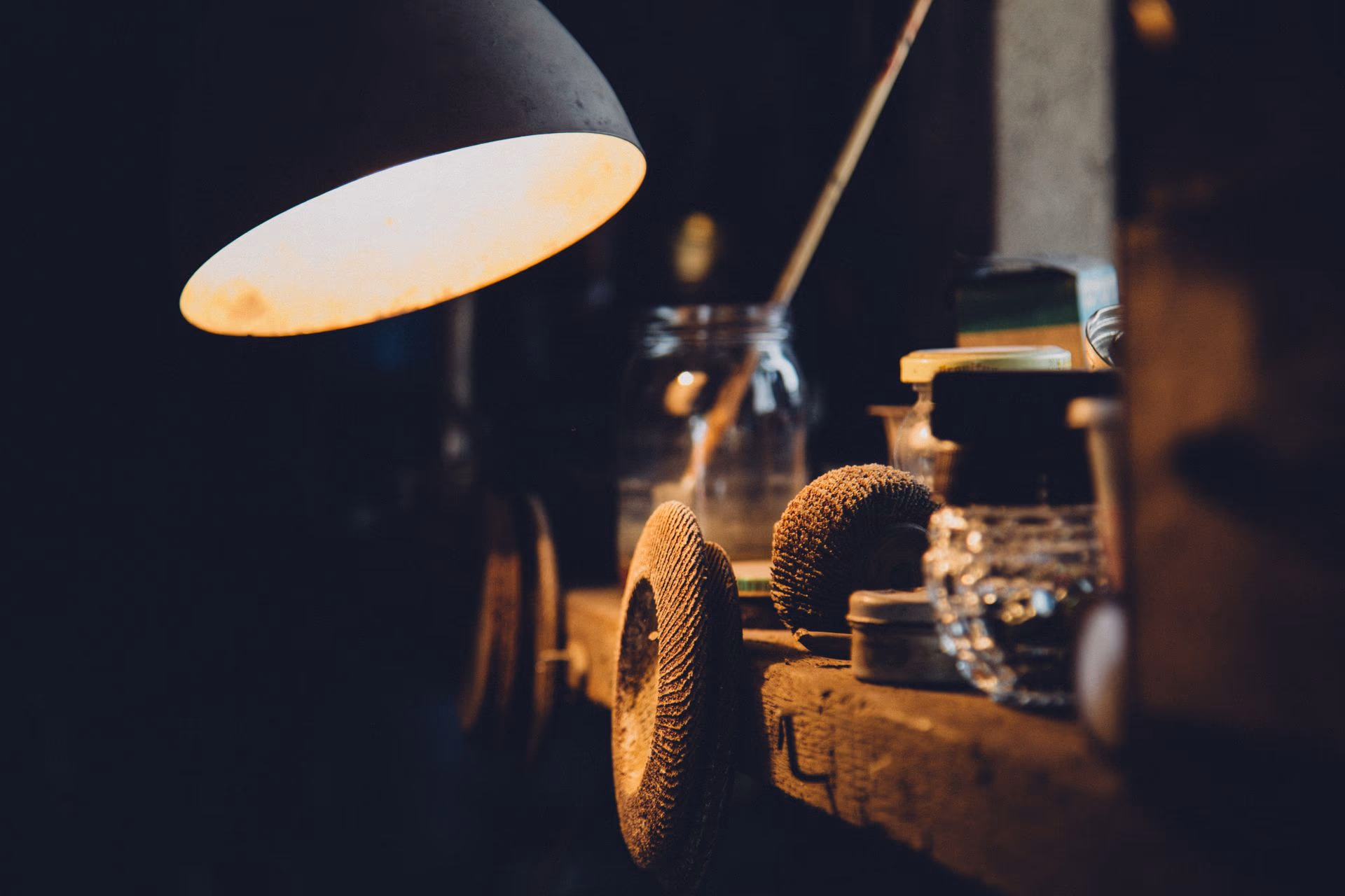 Une lampe d'atelier allumée au-dessus d'un plan de travail, halo chaud isolé dans la pénombre bleu nuit.