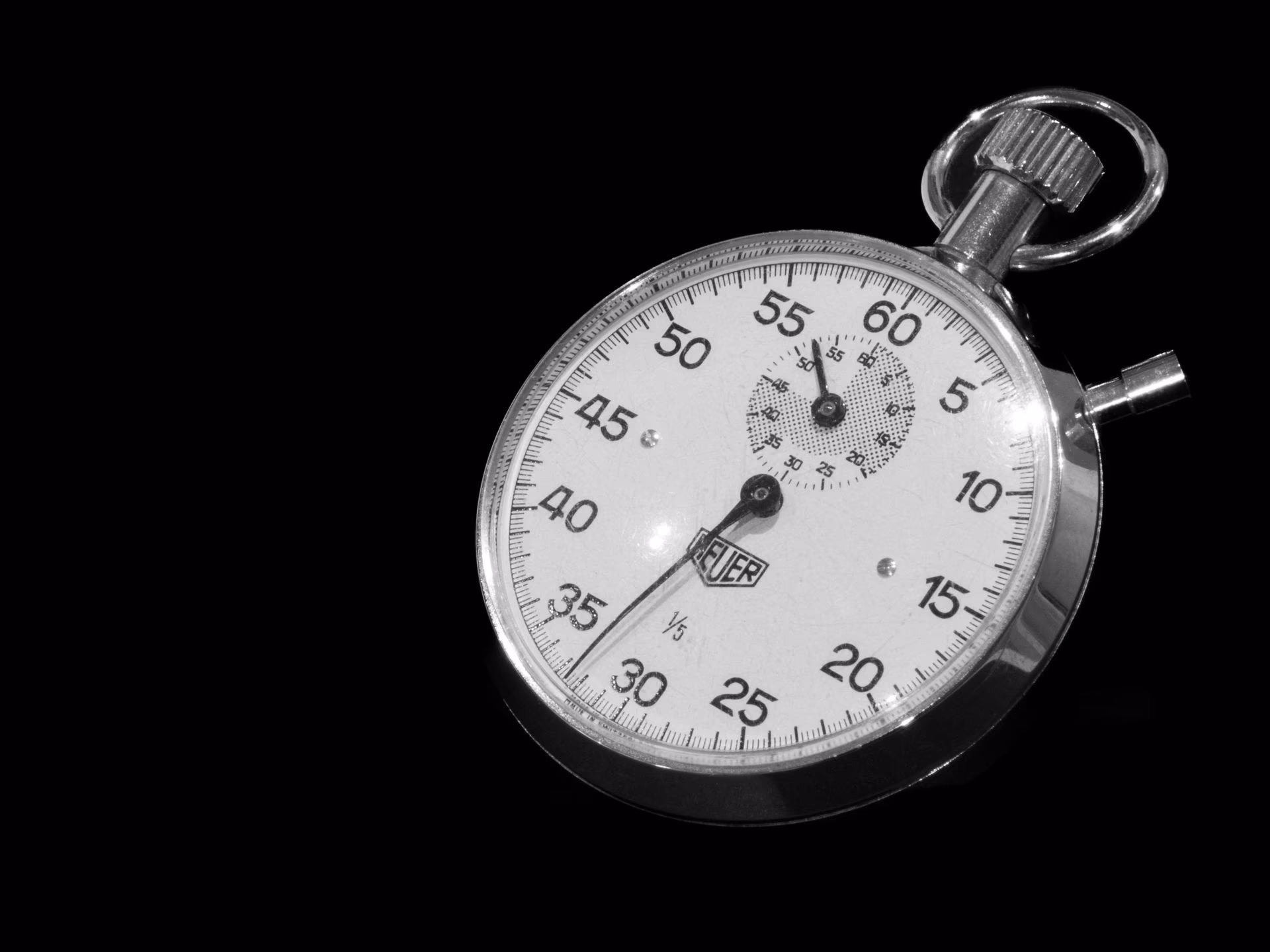 Gros plan d'un chronomètre mécanique, cadran et couronne nets sur fond sombre, hautes lumières laiton et crème.